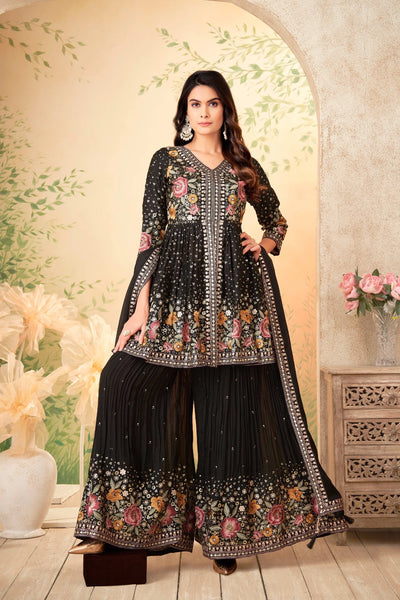 Woman wearing a black embroidered sharara suit traditional outfit with floral patterns indoors.