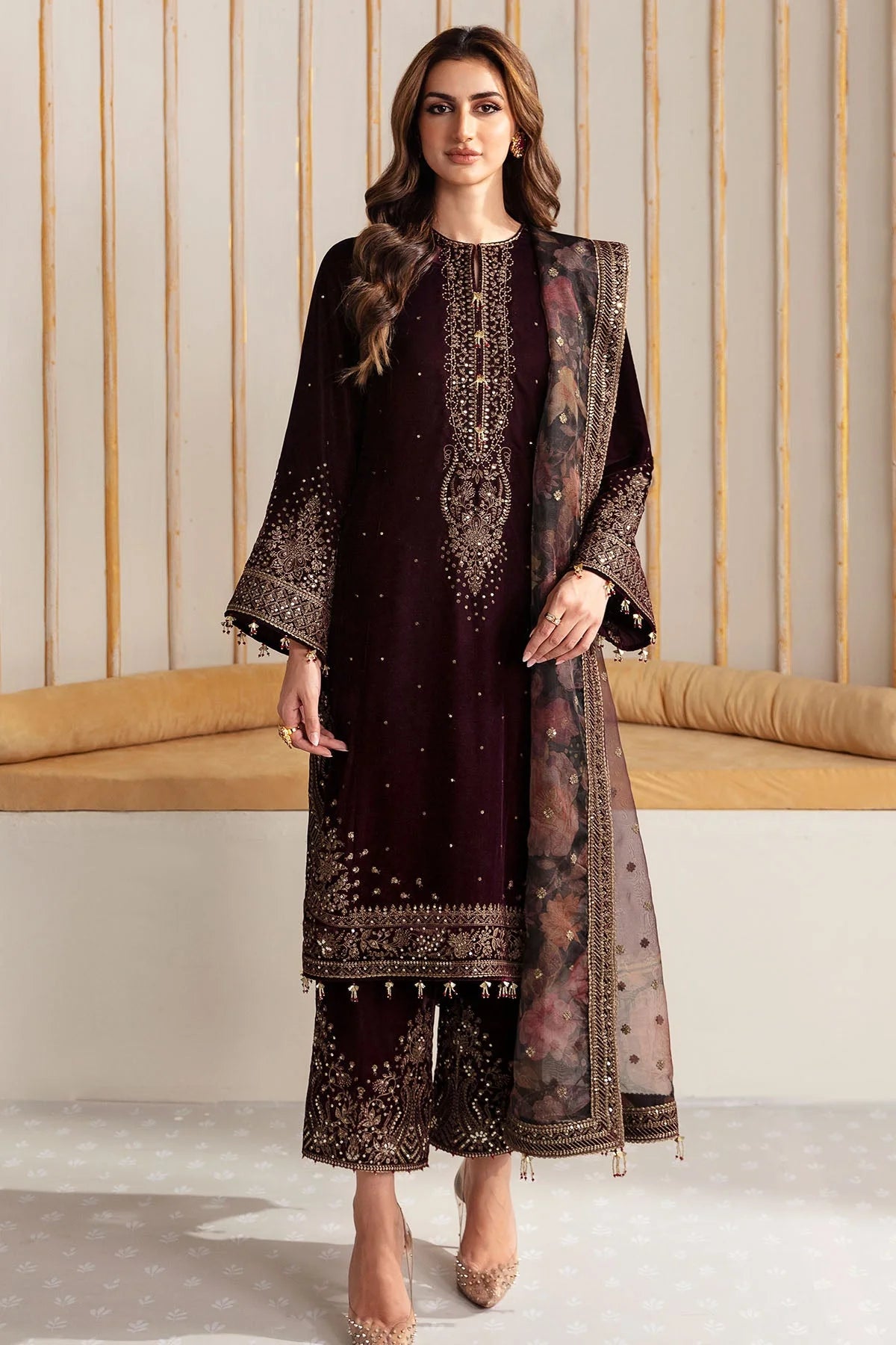 Woman wearing an embroidered velvet traditional outfit with a sheer dupatta against a neutral background