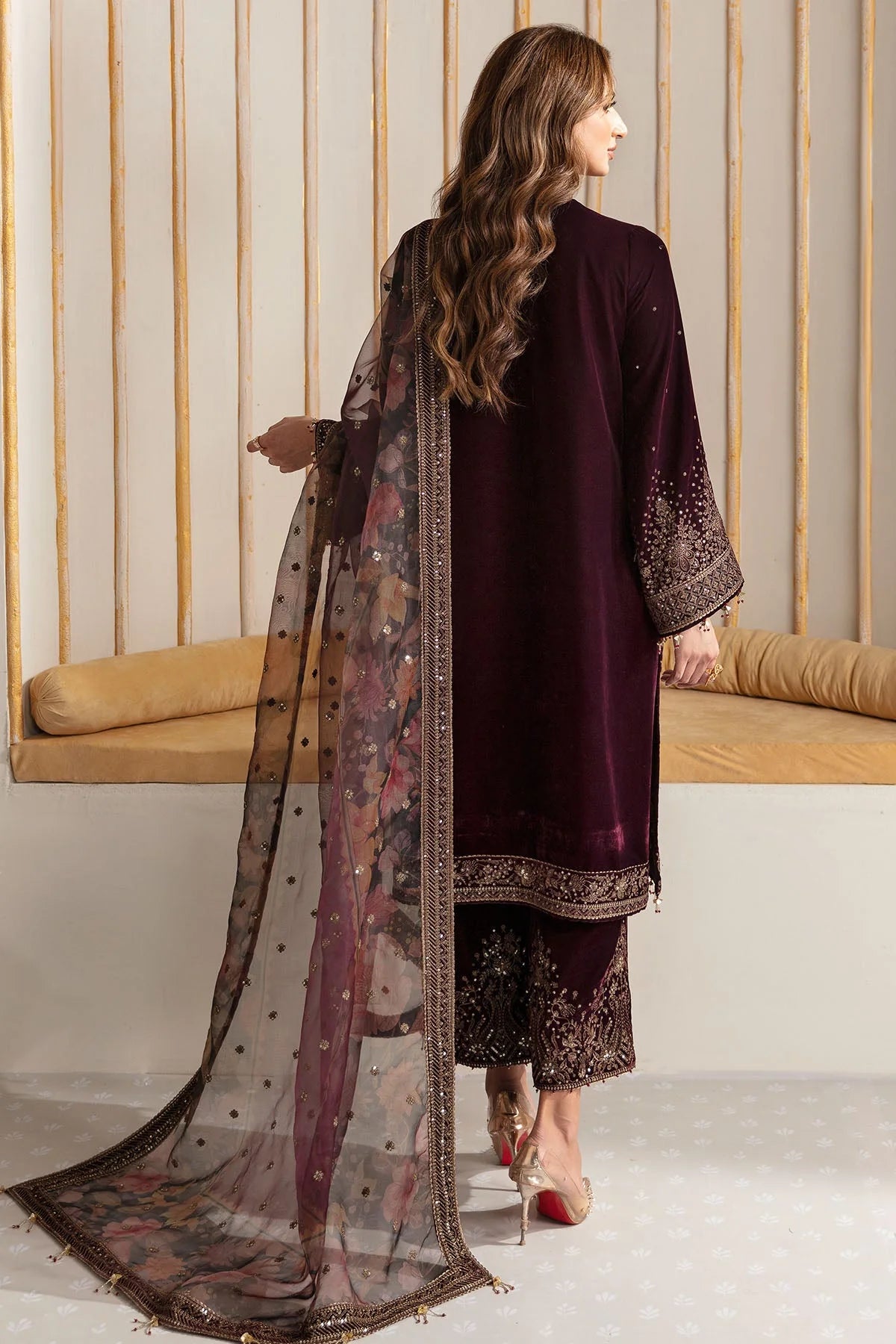 Woman wearing an embroidered velvet traditional outfit with a sheer dupatta against a neutral background