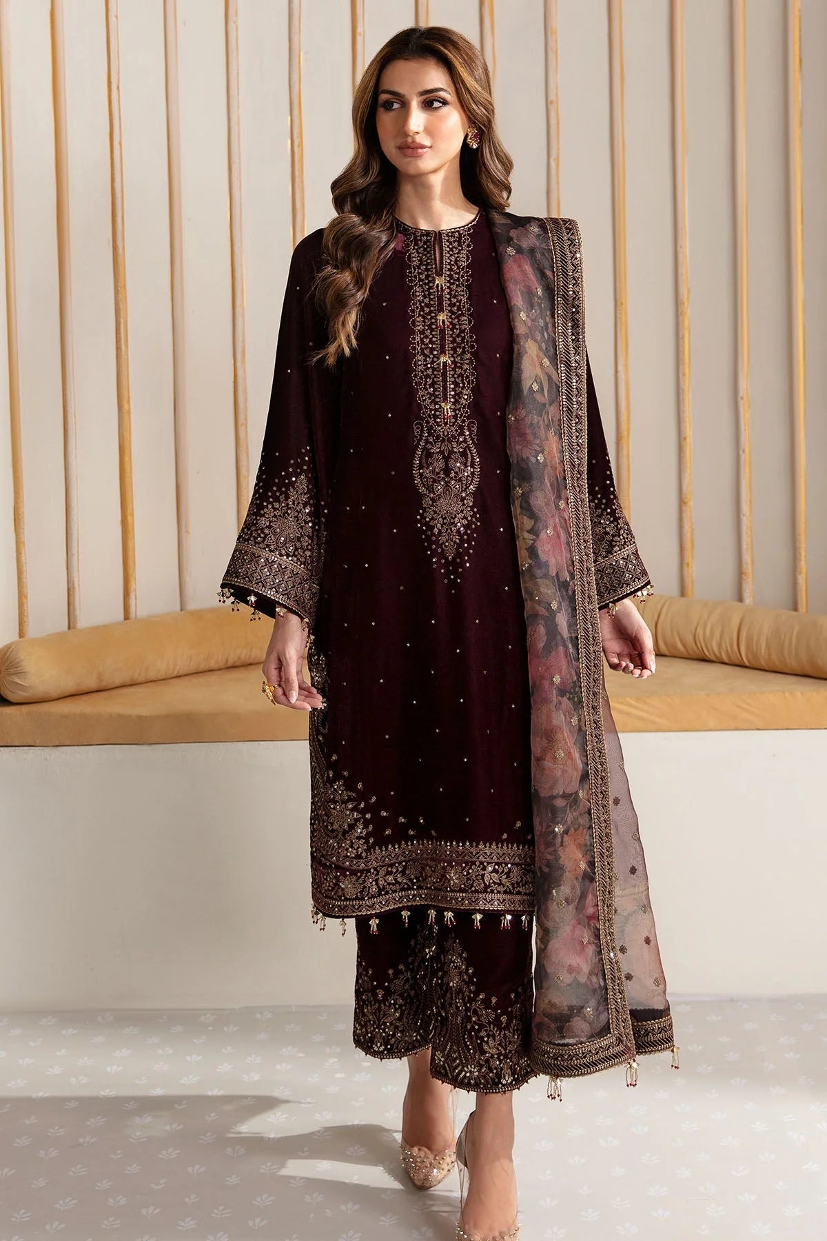 Woman wearing an embroidered velvet traditional outfit with a sheer dupatta against a neutral background