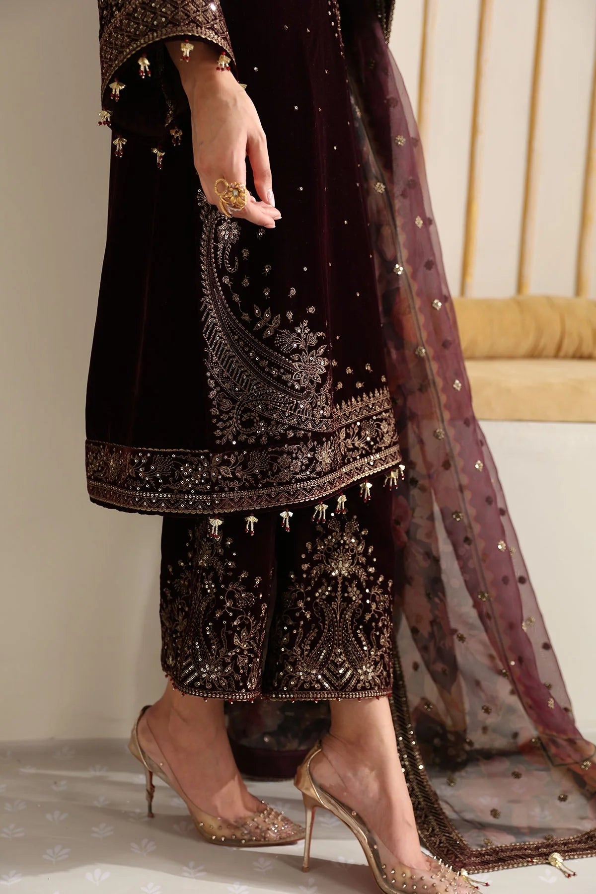 Woman wearing an embroidered velvet traditional outfit with a sheer dupatta against a neutral background