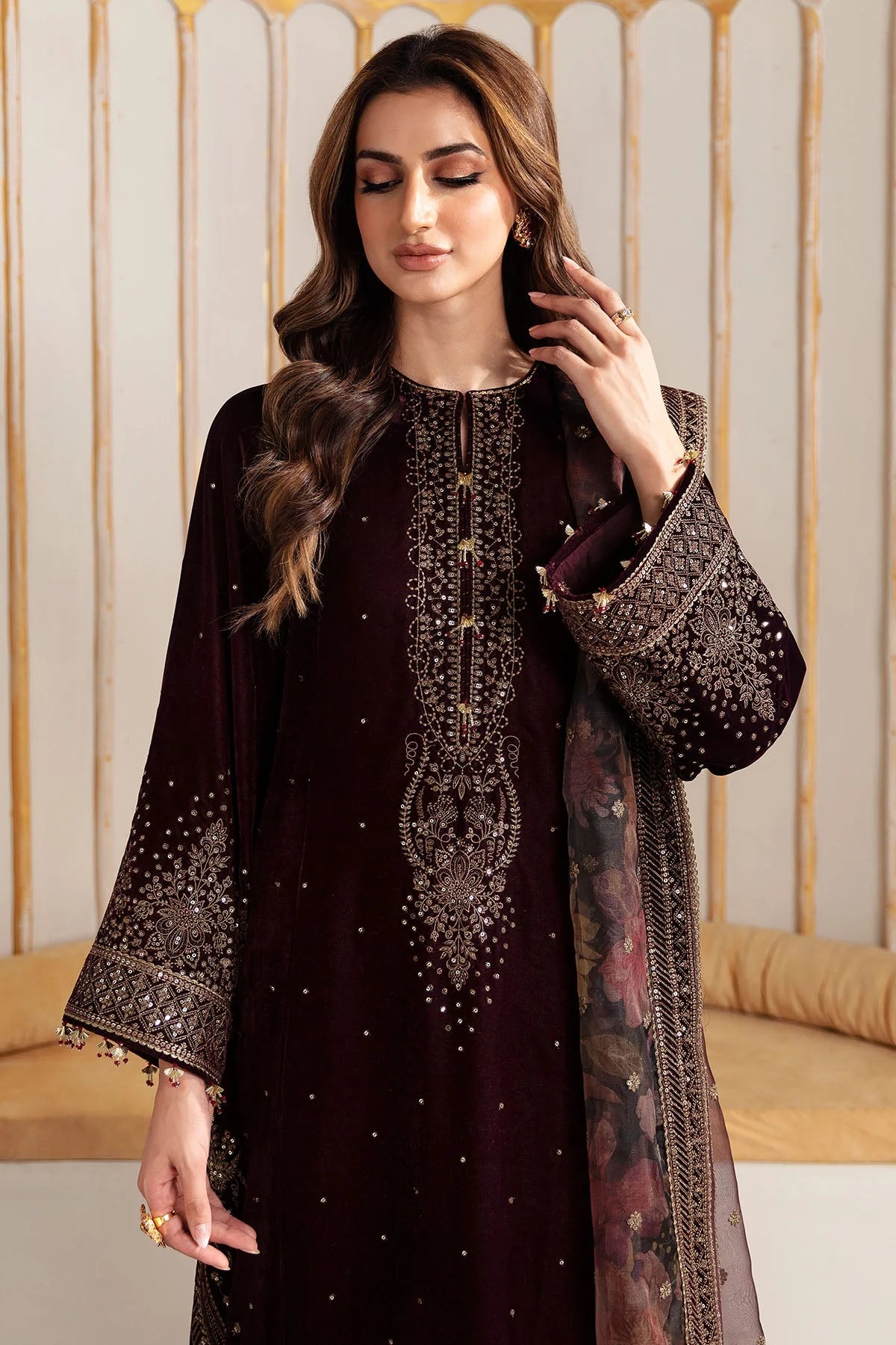 Woman wearing an embroidered velvet traditional outfit with a sheer dupatta against a neutral background