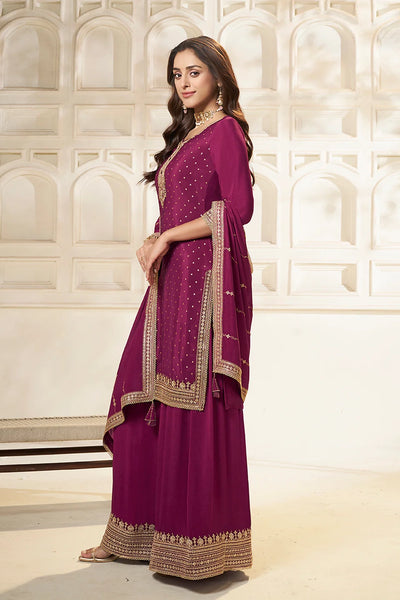 Woman wearing a purple plum sharara suit traditional outfit with gold embroidery in an elegant setting.Woman wearing a purple plum sharara suit traditional outfit with gold embroidery in an elegant setting.