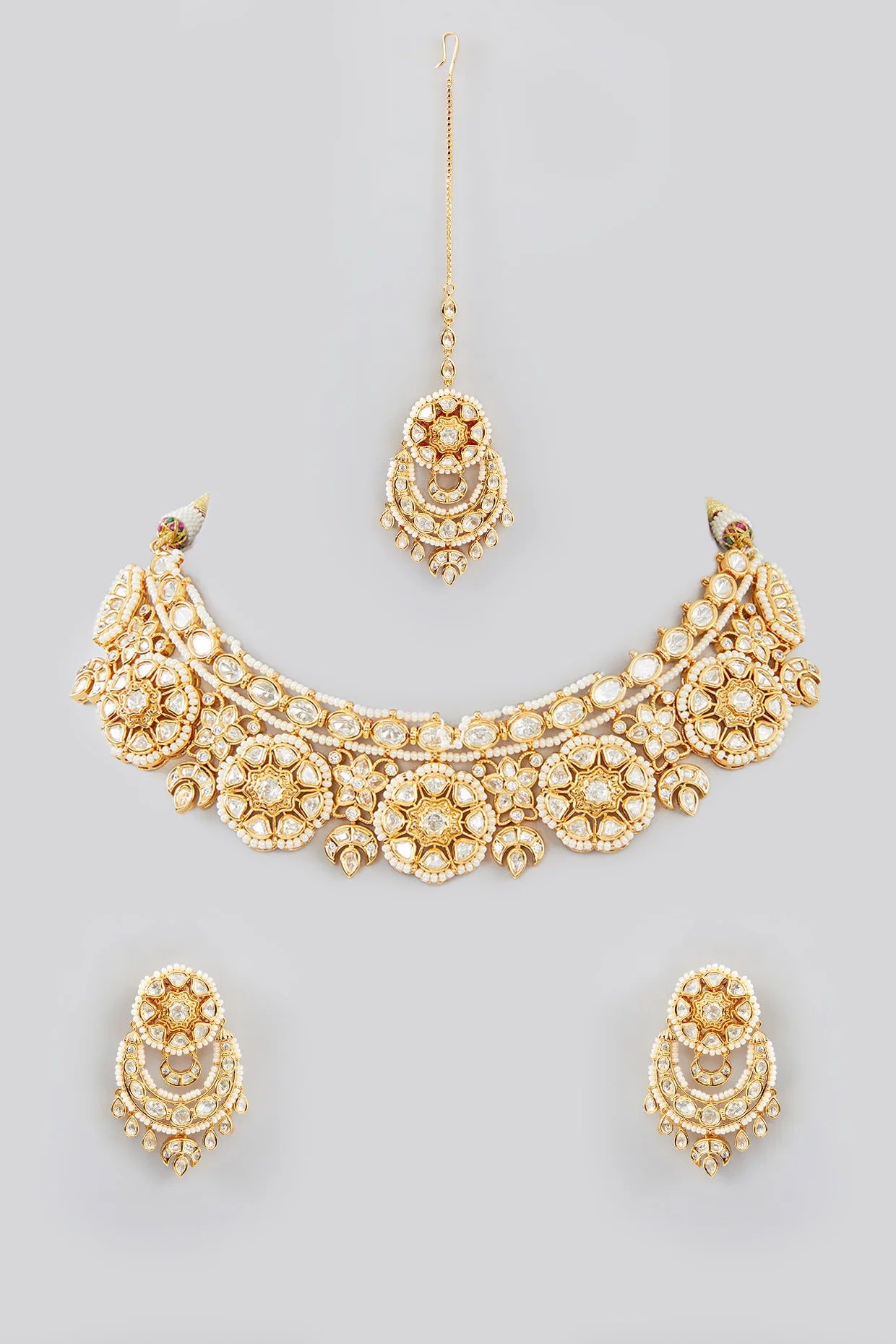 Gold kundan necklace and earrings set on a gray background