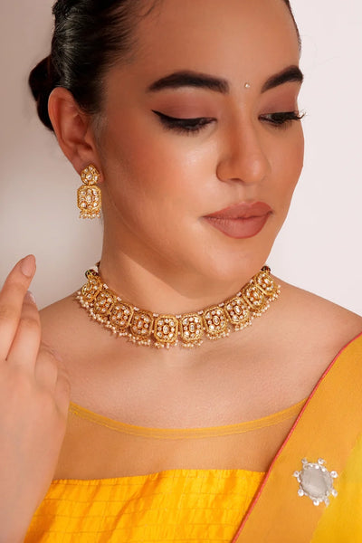 Woman wearing traditional gold kundan & pearl jewelry including a necklace and earrings, with a plain background