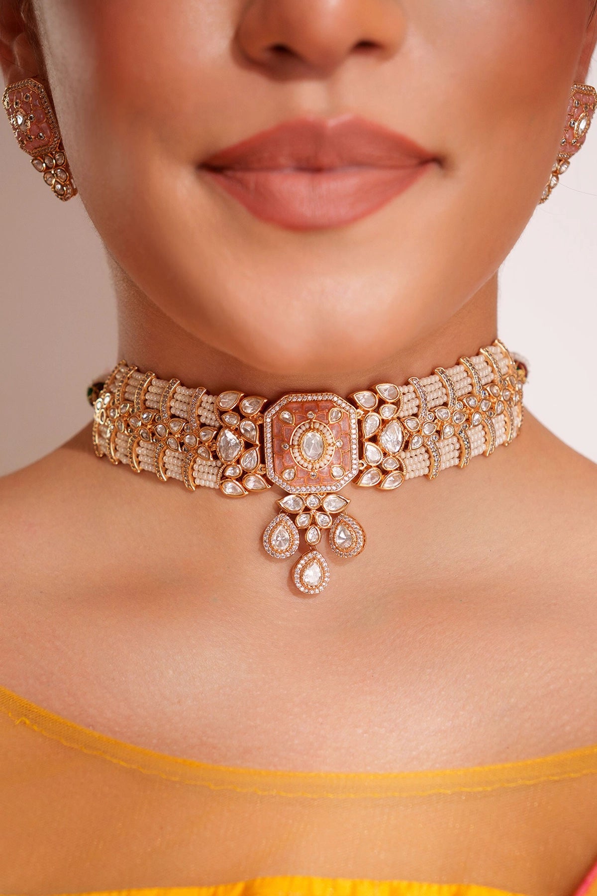 Close-up of a woman wearing a sparkling cPeach Pink Kundan Choker Set necklace and earrings.