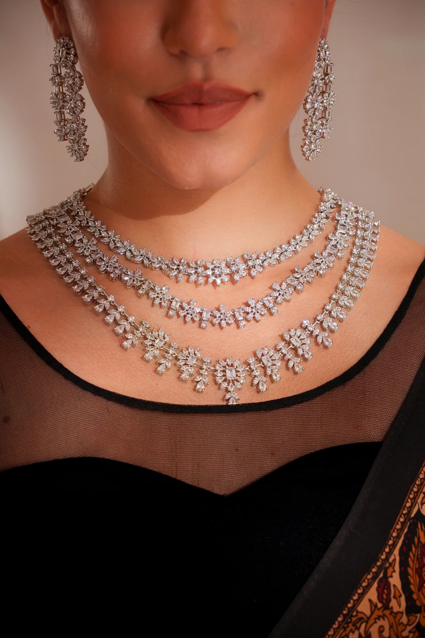 Close-up of a person wearing a silver necklace and earrings on a neutral background