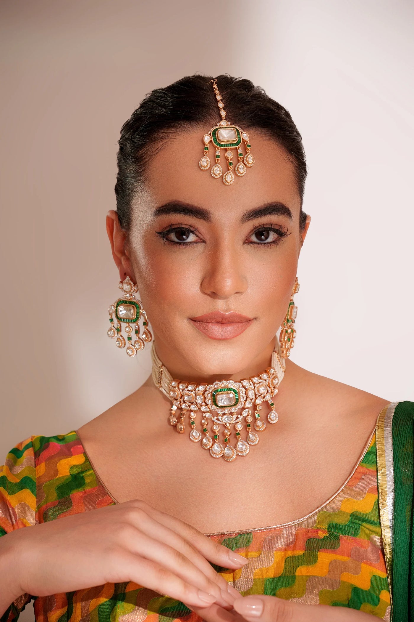 Woman wearing traditional kundan jewelry with a colorful suit against a neutral background