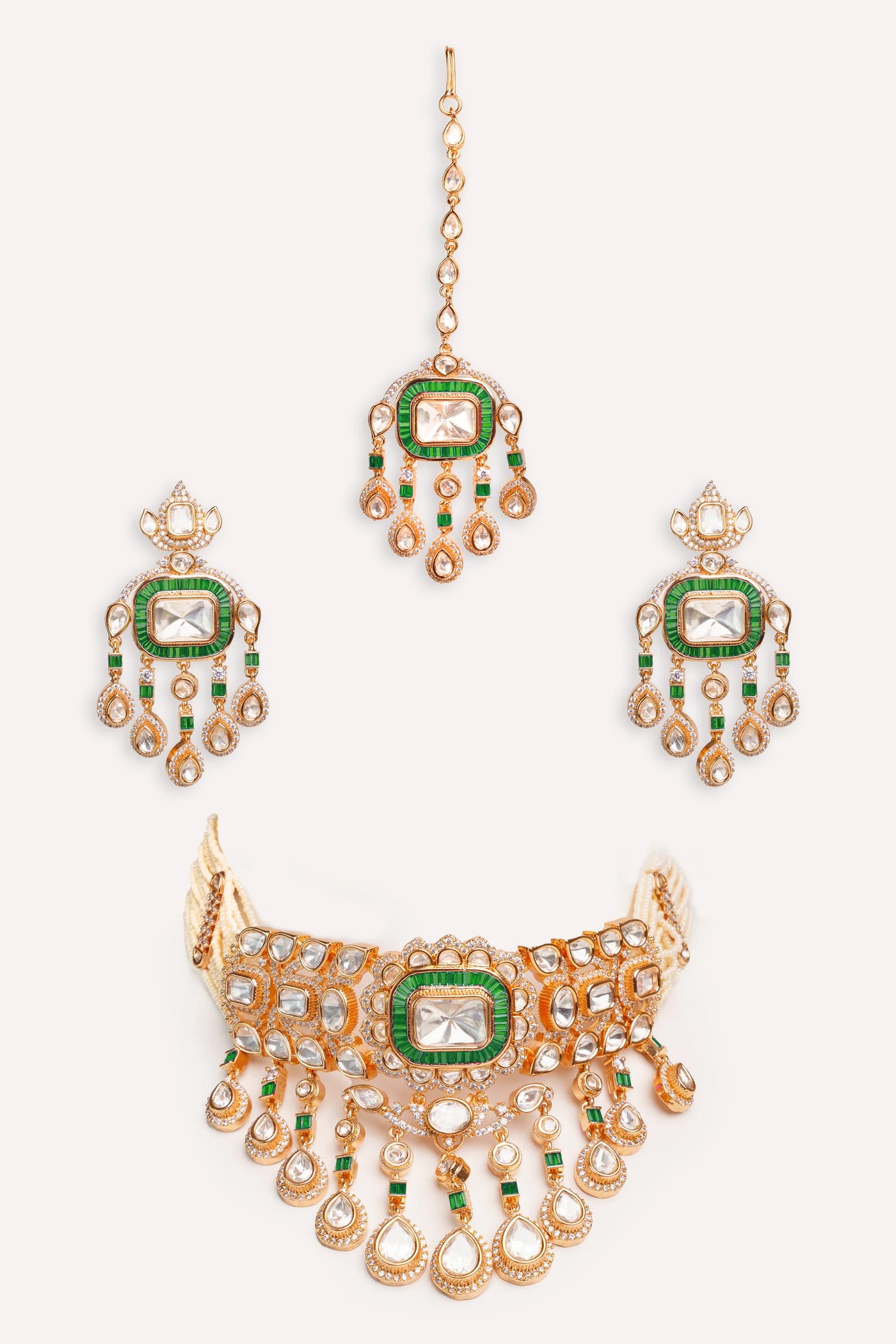Gold Kundan necklace and earrings with green gemstones on a white background