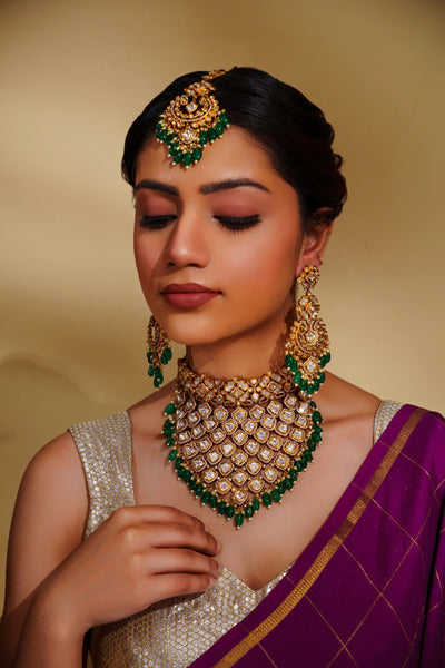 Woman wearing traditional polki jewelry and a saree with a gold and green necklace.