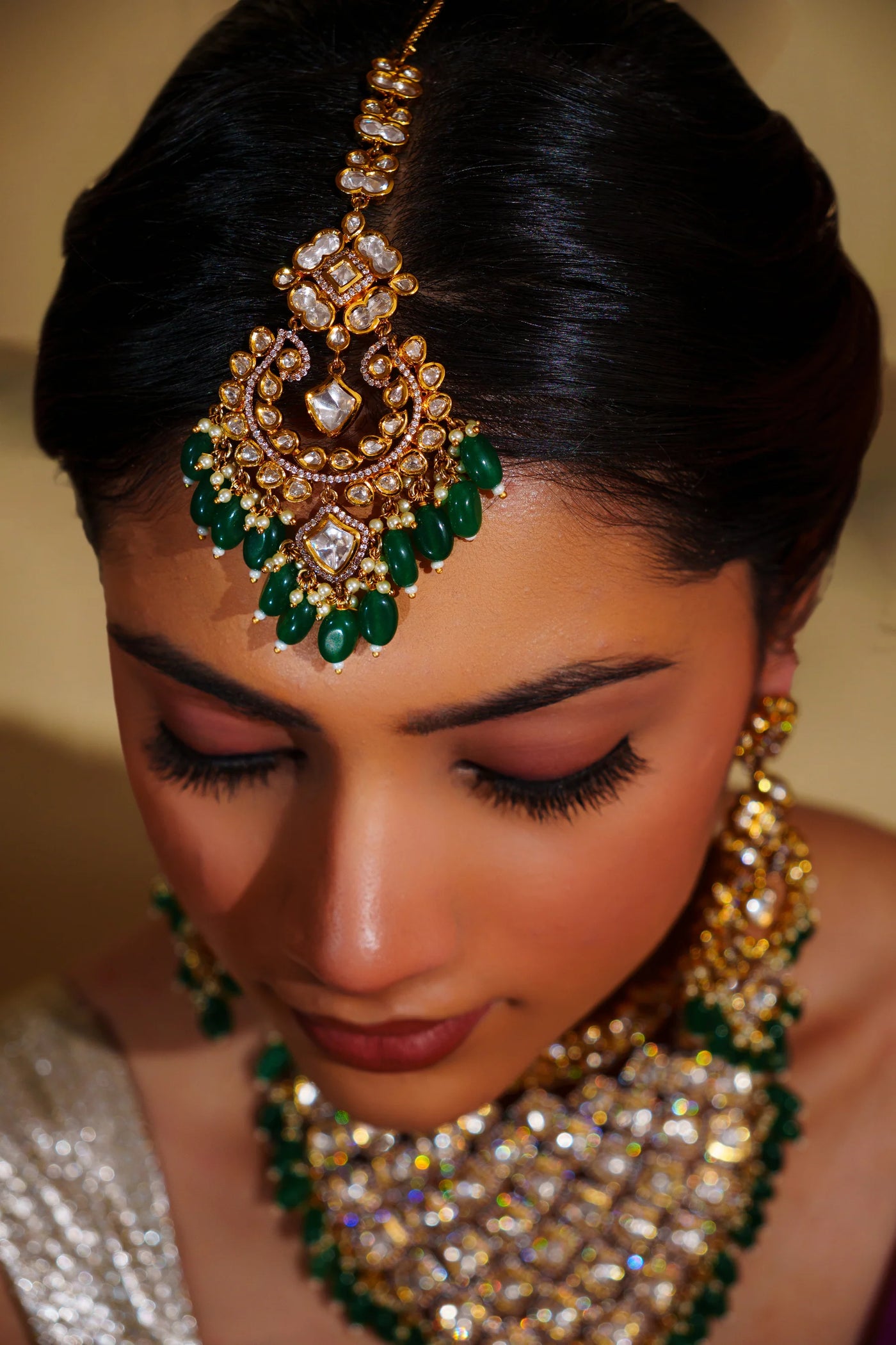 Woman wearing elaborate gold and green kundan jewelry with a blurred background