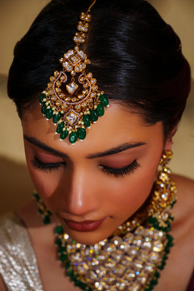 Woman wearing elaborate gold and green kundan jewelry with a blurred backgroundWoman wearing elaborate gold and green kundan jewelry with a blurred background
