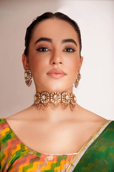 Woman wearing traditional jewelry and a saree against a plain background