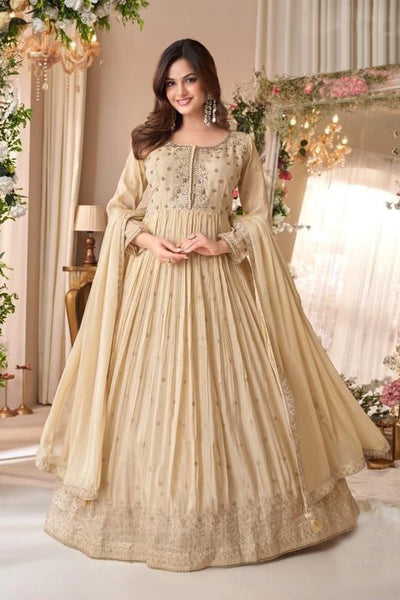 Woman in a beige embroidered anarkali dress standing in a decorated indoor setting.