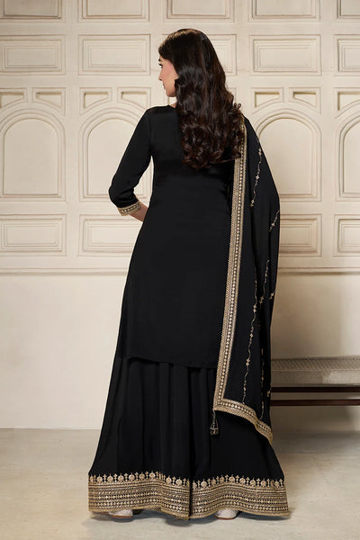 Woman wearing a black sharara suit traditional outfit with gold embroidery in a room with decorative walls.Woman wearing a black sharara suit traditional outfit with gold embroidery in a room with decorative walls.