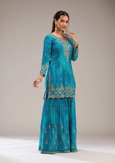 Woman wearing a turquoise embroidered traditional sharara outfit on a plain backgroundWoman wearing a turquoise embroidered traditional sharara outfit on a plain background