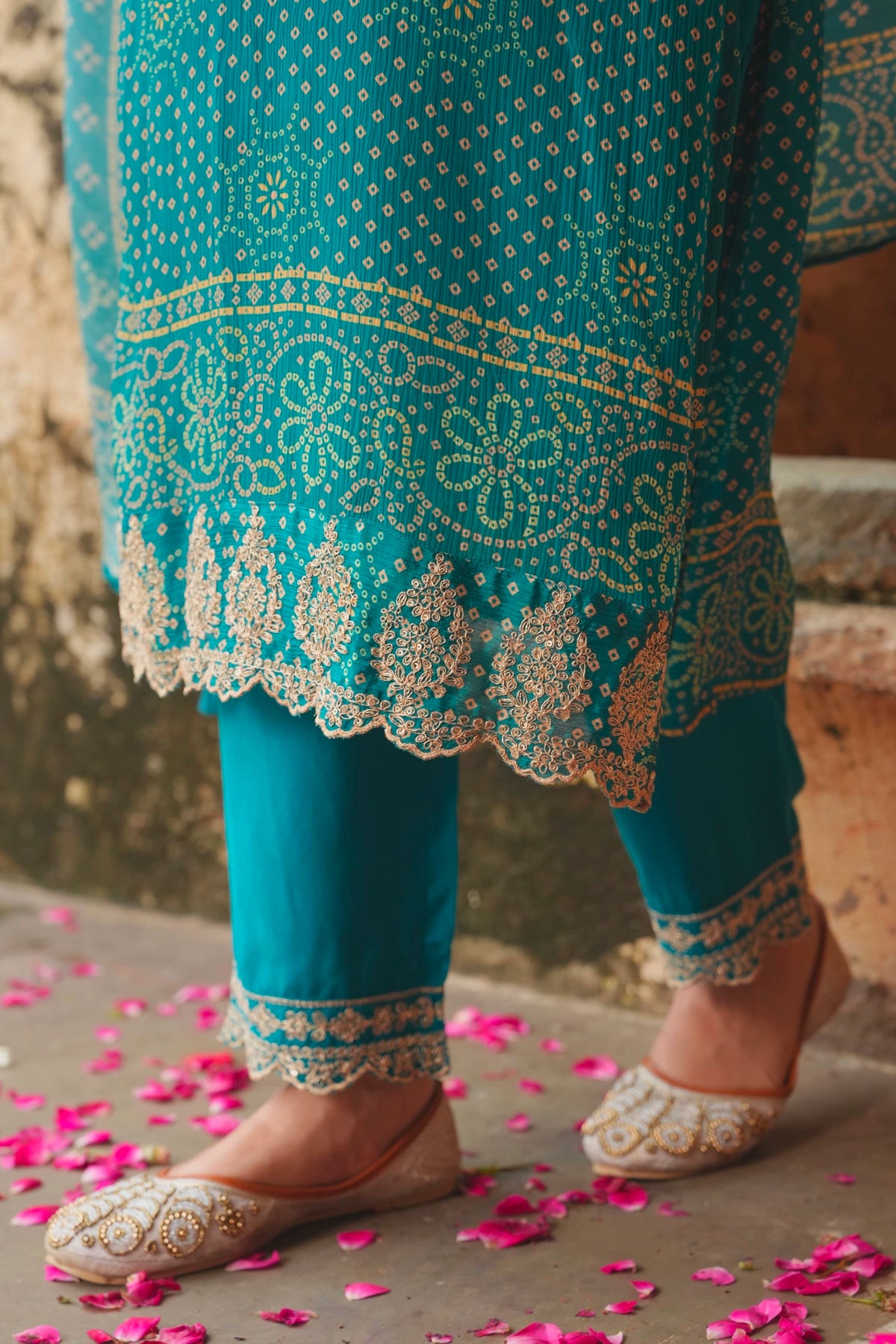 Teal embroidered teal blue outfit with gold details on a stone surface with pink petals.