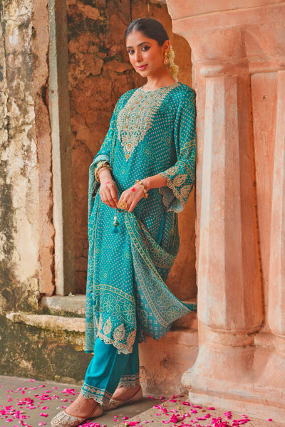 Woman in a teal blue traditional outfit standing in front of stone architecture with pink petals on the ground.Woman in a teal blue traditional outfit standing in front of stone architecture with pink petals on the ground.