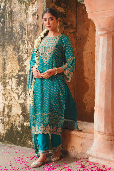 Woman in a teal blue traditional outfit standing in an architectural setting with pink petals on the ground.