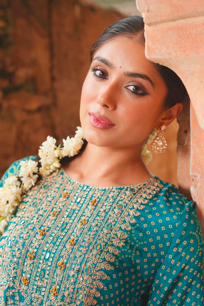 Woman in traditional teal blue attire with floral decorations, standing against a stone wall.Woman in traditional teal blue attire with floral decorations, standing against a stone wall.