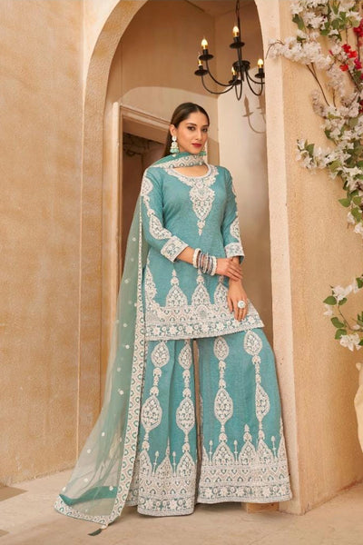 Woman in a traditional blue and white embroidered outfit standing in a decorated hallway.