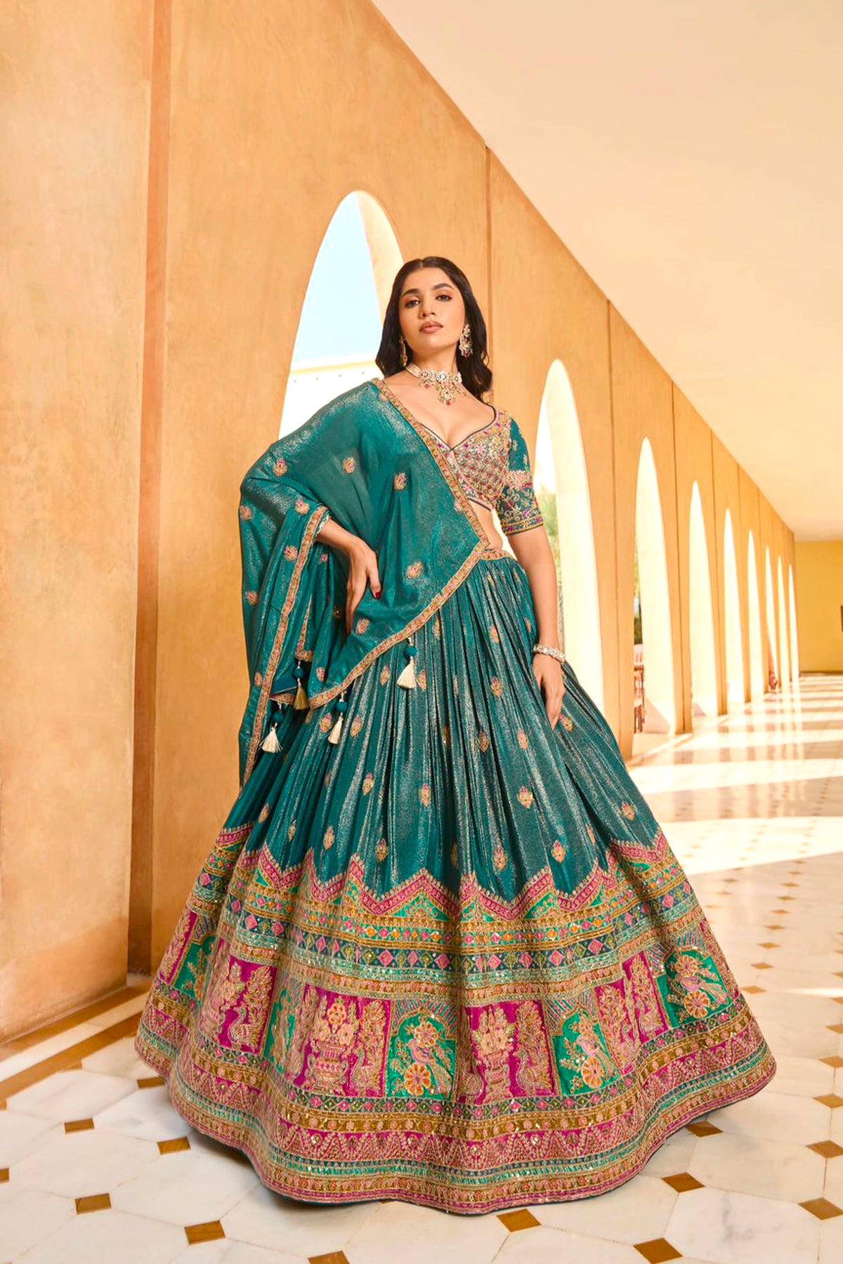 Woman in a traditional green embroidered lehenga set standing in an elegant hallway.