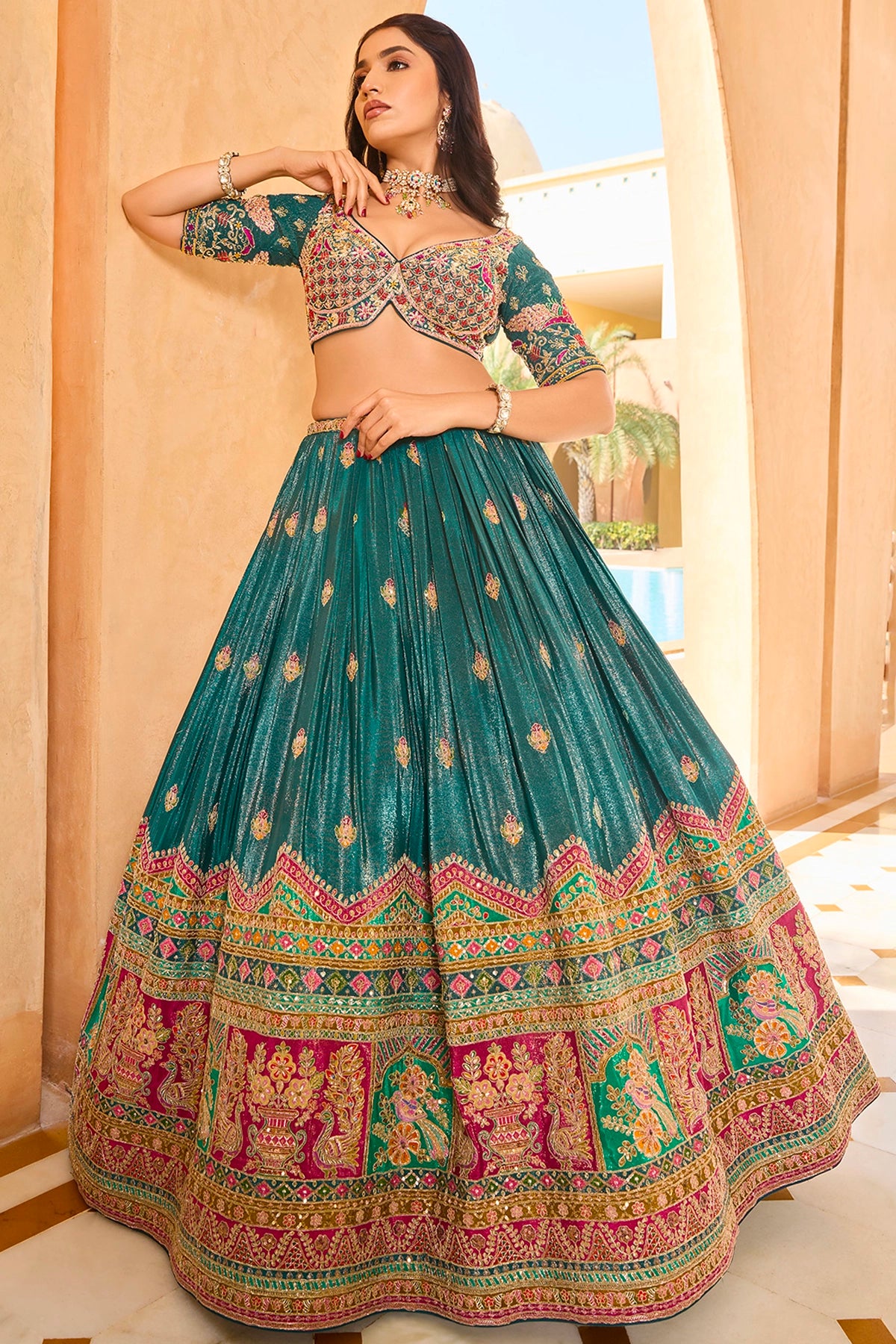 Woman wearing a traditional green and multicolor lehenga with intricate patterns indoors.