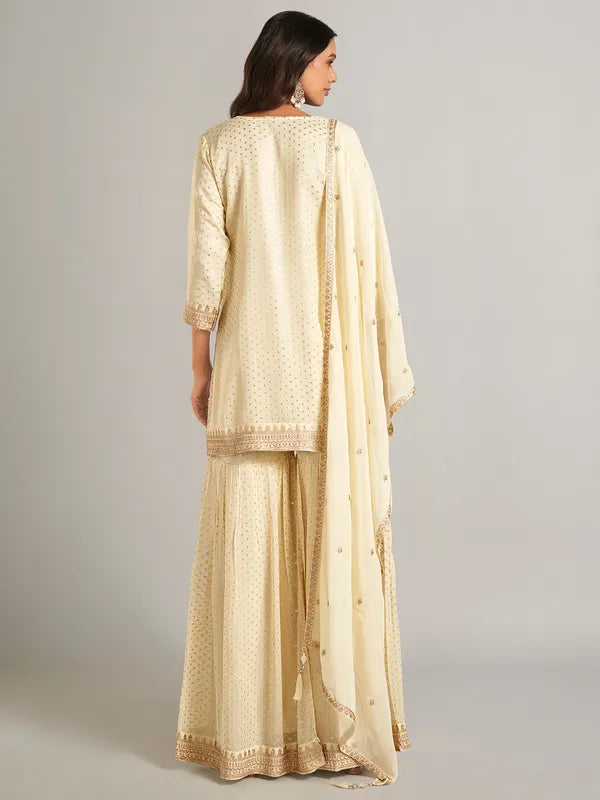 Woman wearing a creme traditional outfit with a matching dupatta on a plain background