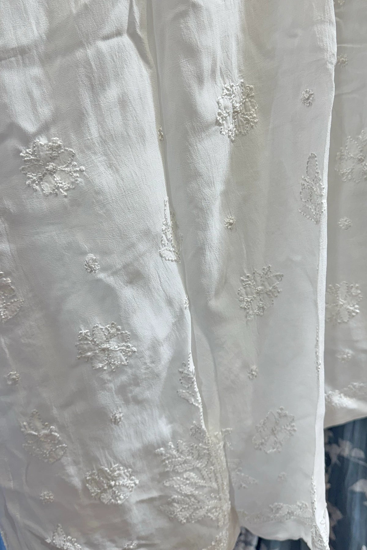 White fabric with intricate  Lucknowi Chikankari embroidery on a plain background