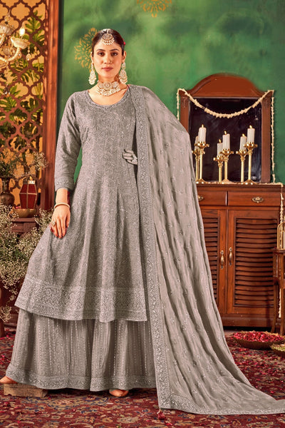 Woman in a gray traditional anarkali outfit with a matching dupatta against a decorative background.Woman in a gray traditional anarkali outfit with a matching dupatta against a decorative background.
