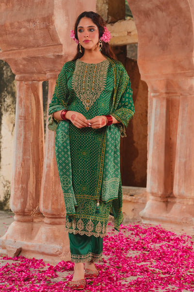 Woman in a green traditional outfit standing on pink petals with architectural columns in the background