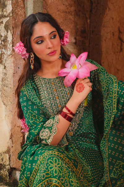 Woman in a green traditional outfit holding pink flowers against a stone wall.Woman in a green traditional outfit holding pink flowers against a stone wall.