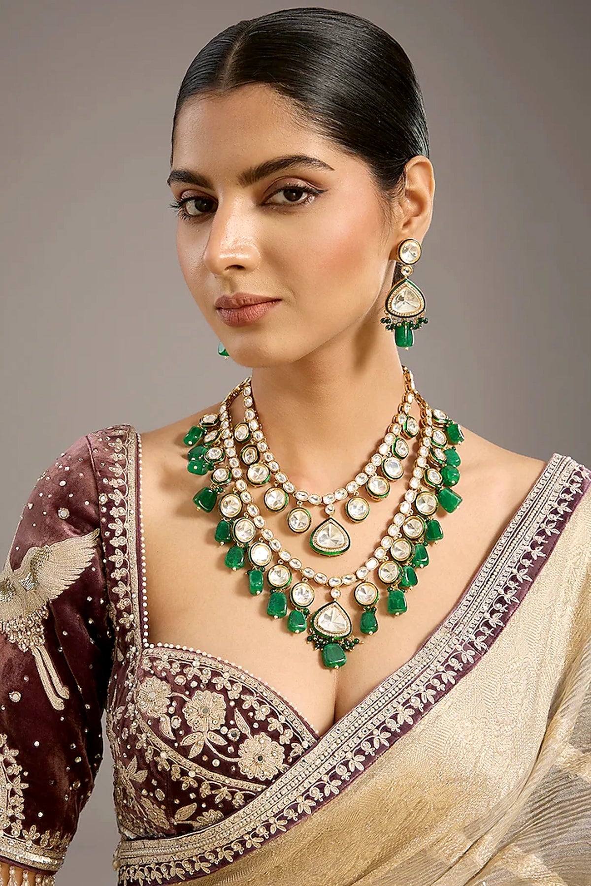 Woman wearing a traditional saree with green and gold jewelry kundan set against a neutral background