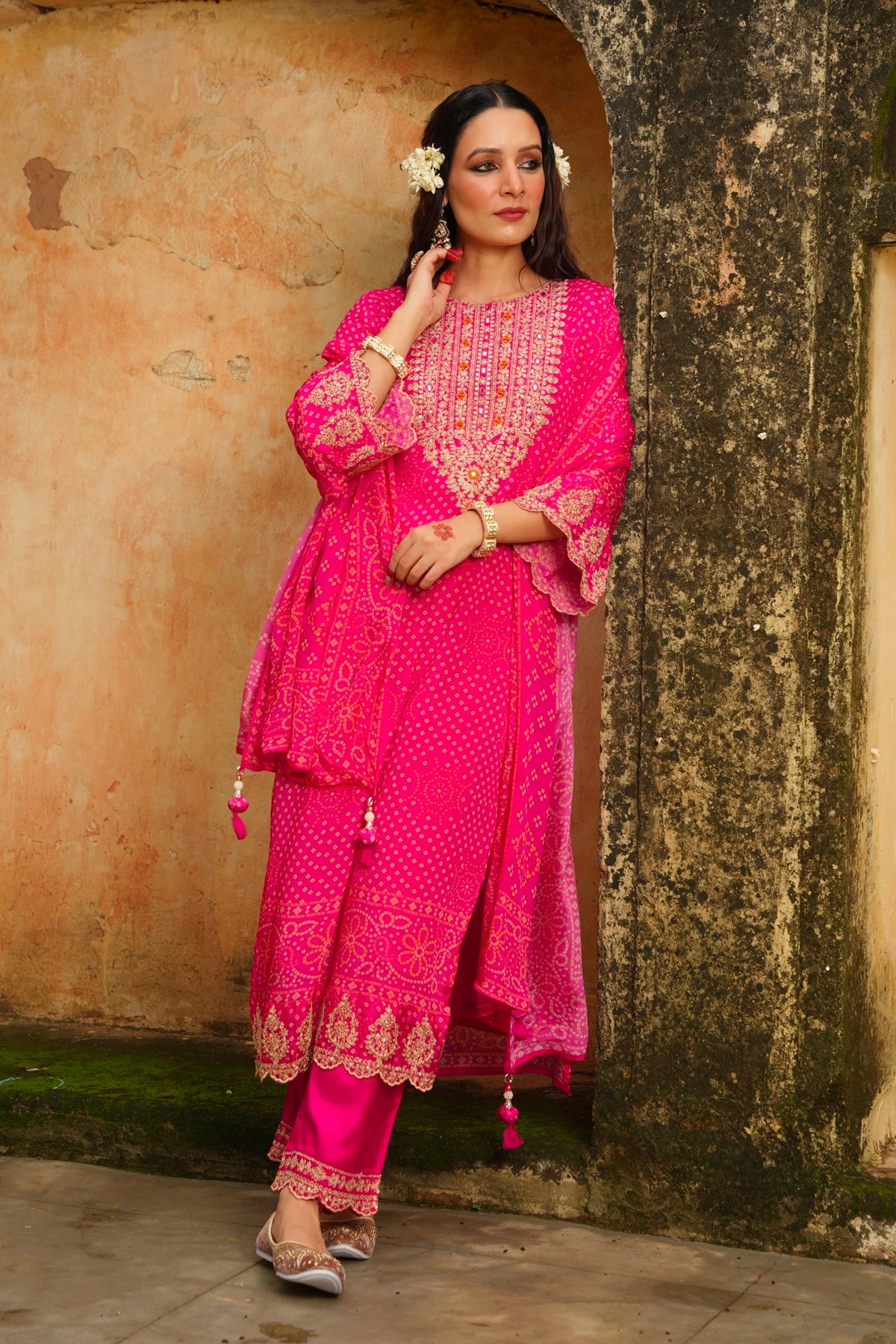 Woman in a bright pink traditional outfit standing against a textured wall.