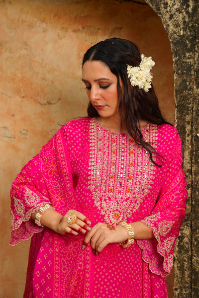 Woman wearing a pink traditional outfit with intricate designs, standing against a textured wall.Woman wearing a pink traditional outfit with intricate designs, standing against a textured wall.