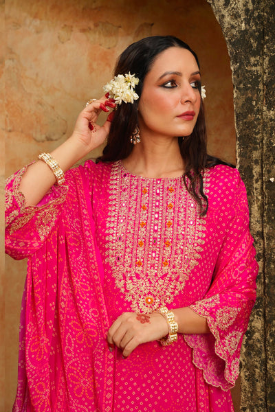 Woman in a pink traditional kurta set outfit with gold embroidery, standing against a textured wall.Woman in a pink traditional kurta set outfit with gold embroidery, standing against a textured wall.