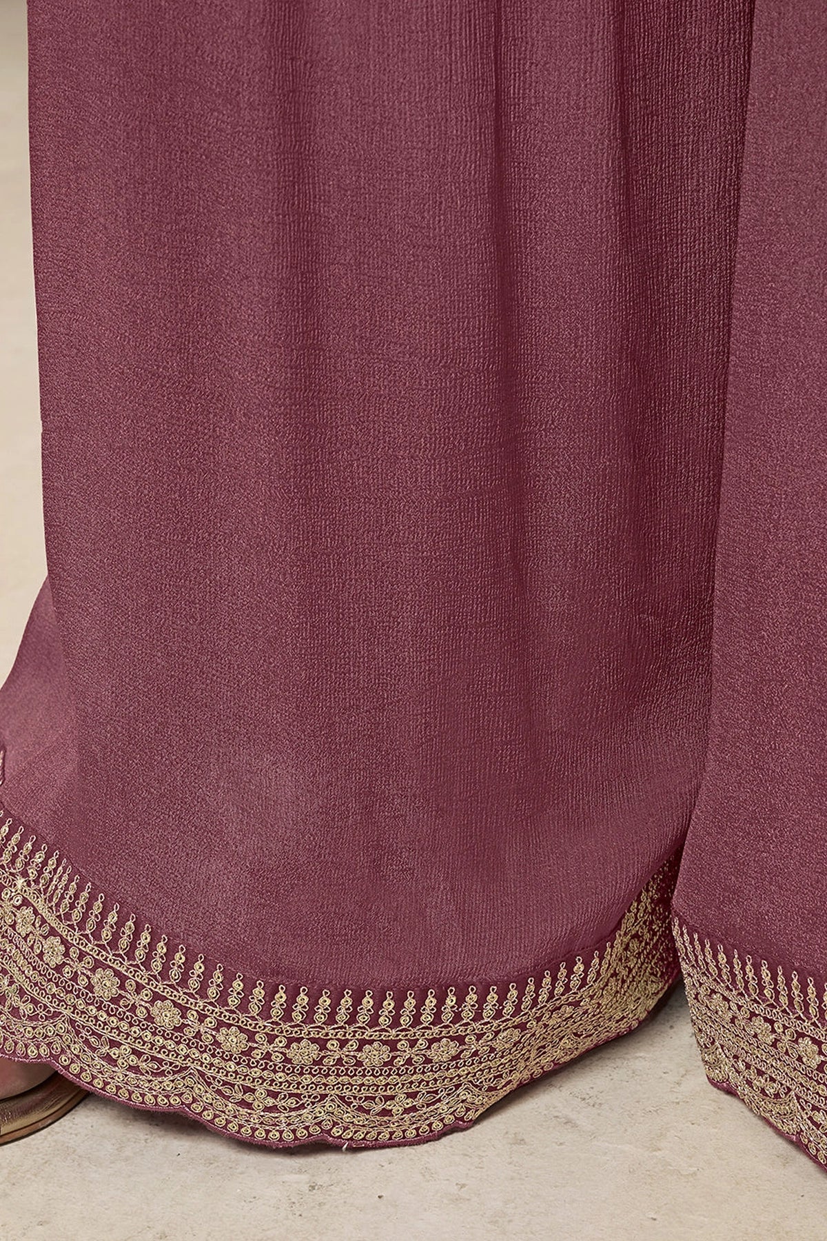 Close-up of a mauve fabric with gold embroidery on a neutral background