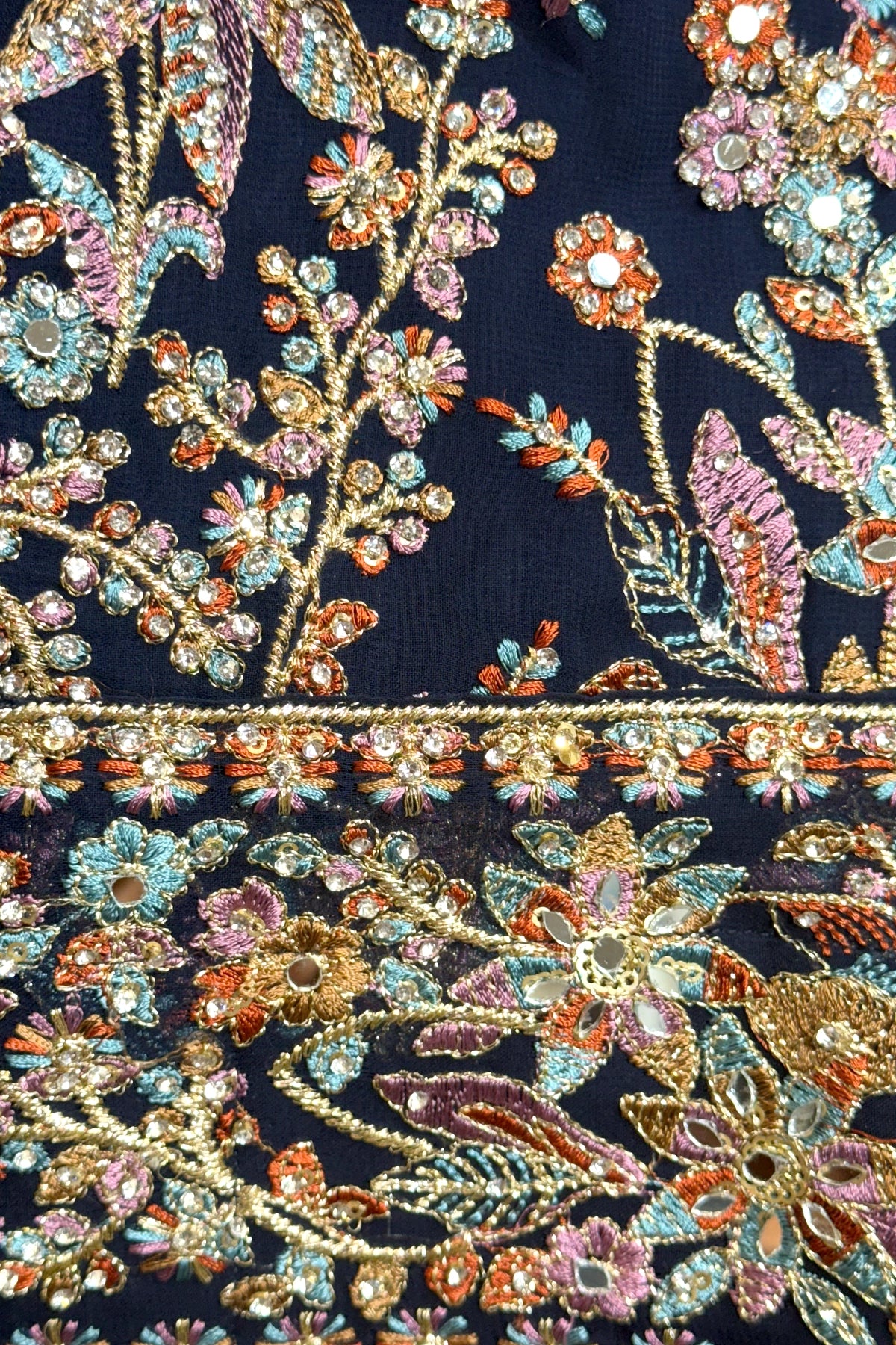 Close-up of a embroidered georgette fabric with floral patterns and multicolored beads on a dark background.