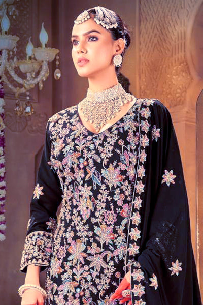 Woman wearing a navy embroidered kurta set outfit with jewelry in a decorative settingWoman wearing a navy embroidered kurta set outfit with jewelry in a decorative setting