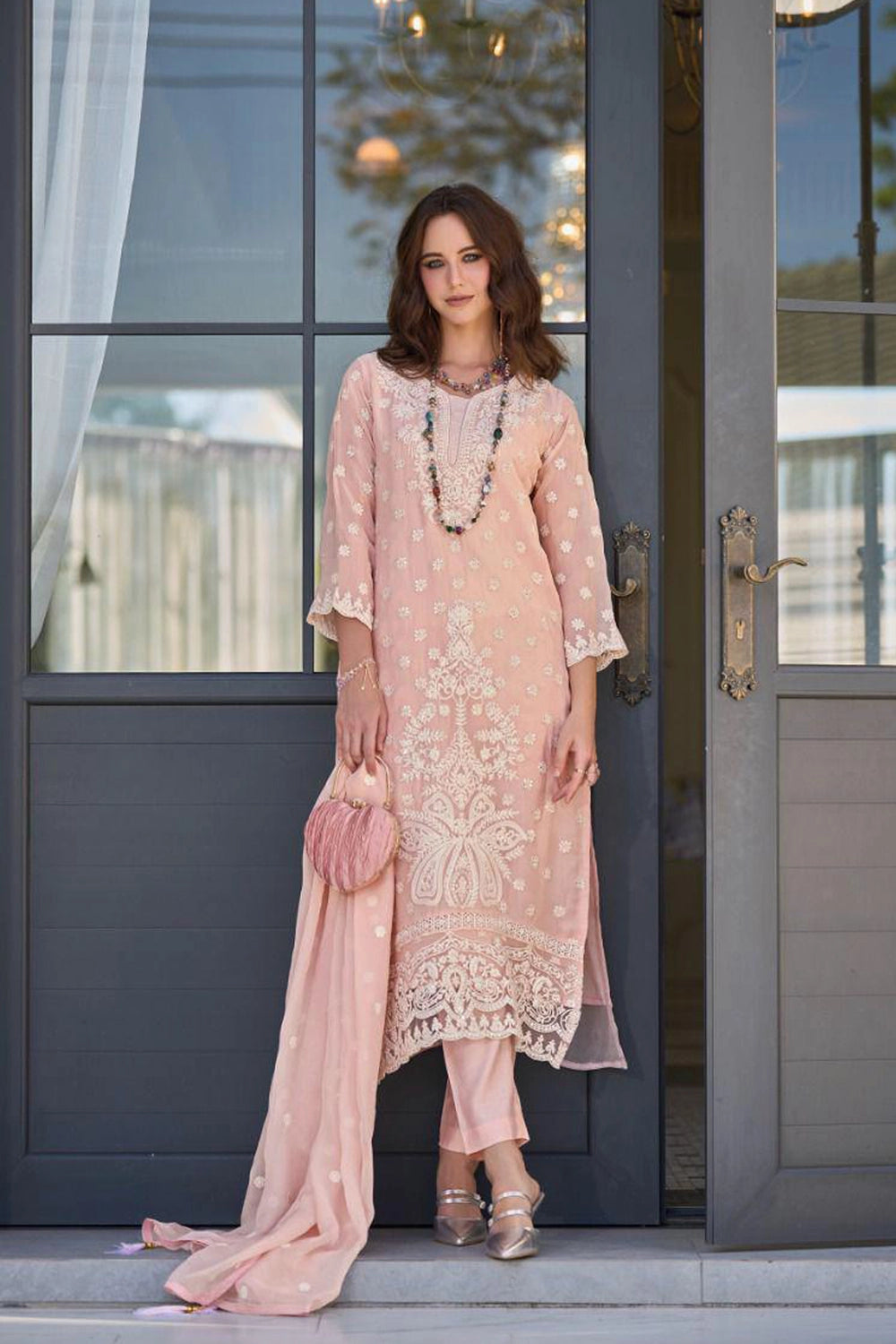 Woman in a peach pink embroidered kurta set standing in front of a gray door.