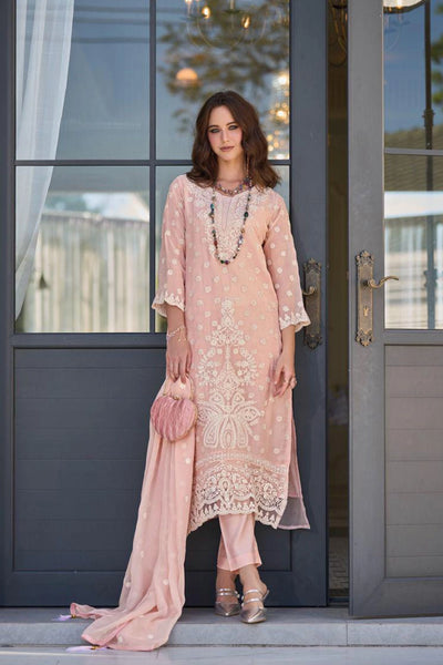 Woman in a peach pink embroidered kurta set standing in front of a gray door.