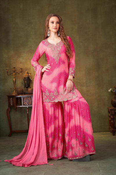 Woman in a pink traditional sharara suit outfit with intricate designs against a neutral background