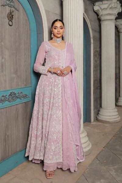 Woman in a pink traditional anarkali outfit standing in an architectural setting.