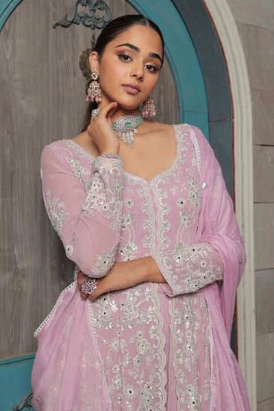 Woman in a pink anarkali embroidered outfit with jewelry against a decorative wall.Woman in a pink anarkali embroidered outfit with jewelry against a decorative wall.