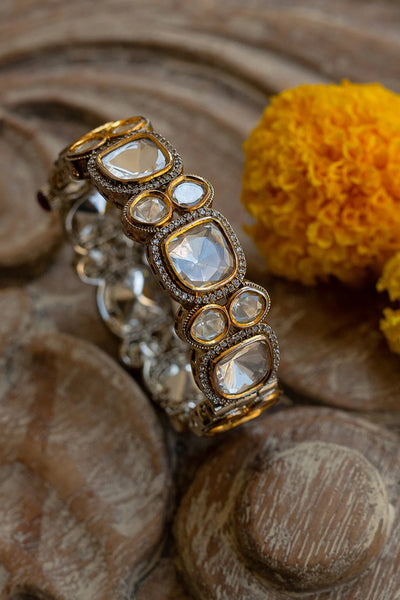 Silver and gold bracelet with polki stones on a wooden surface with a yellow flower.