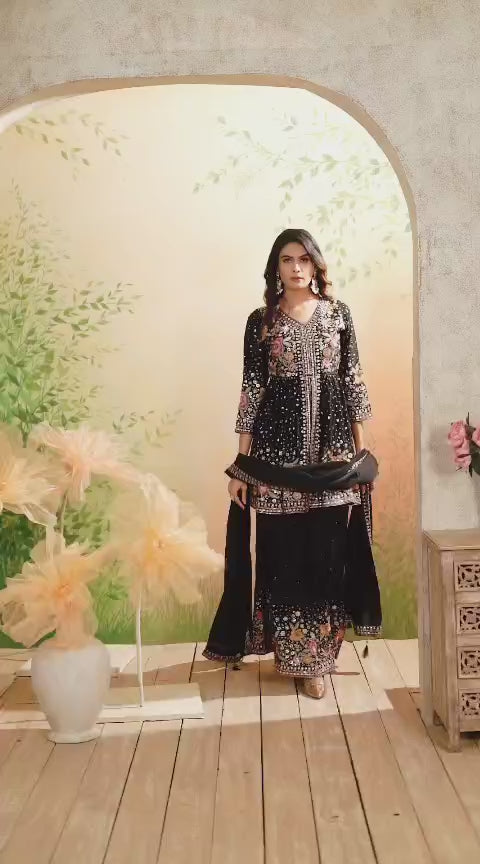 Video of Woman wearing a black embroidered sharara suit traditional outfit with floral patterns indoors.
