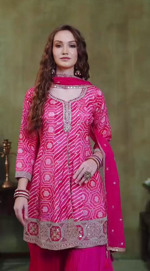 Woman wearing a bright pink traditional outfit with intricate patterns against a green background