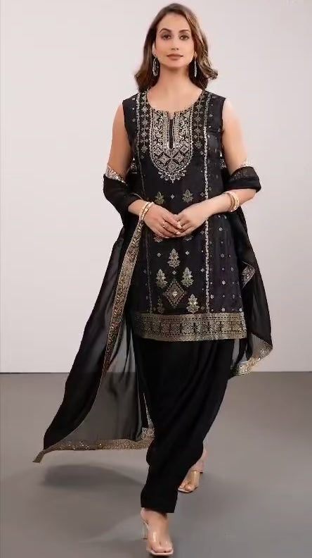 Woman wearing a black traditional patiala salwar suit outfit with intricate embroidery on a gray background