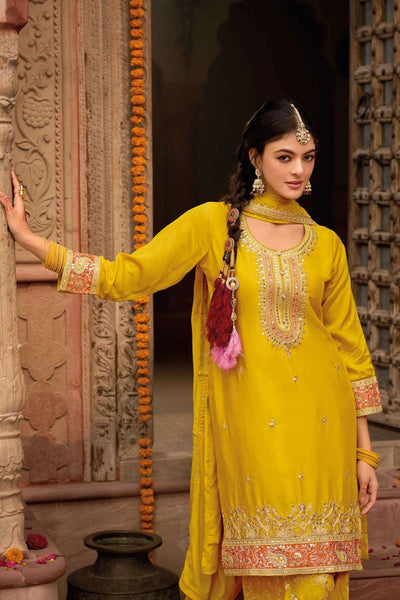 Woman in a yellow traditional punjabi outfit with intricate designs standing in front of an ornate stone wall.Woman in a yellow traditional punjabi outfit with intricate designs standing in front of an ornate stone wall.