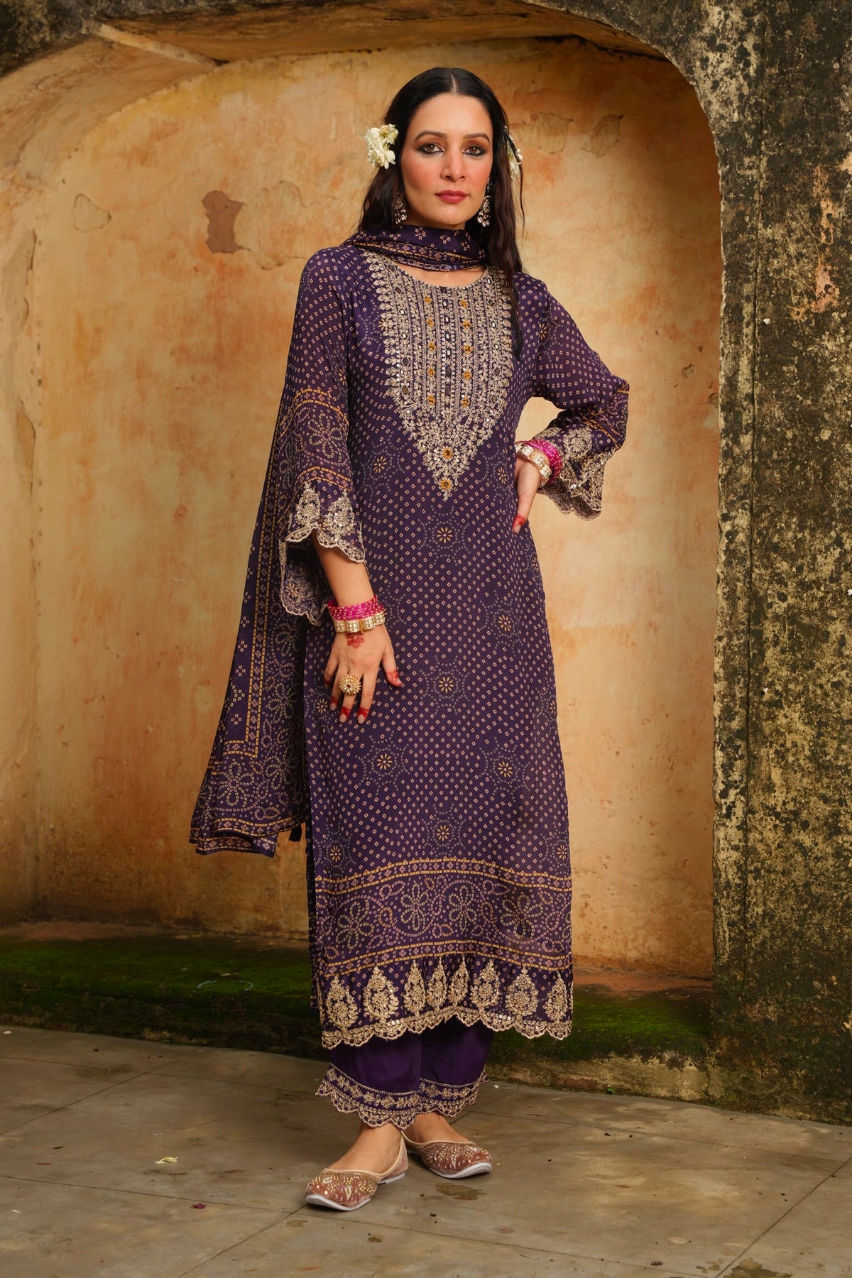 Woman in a traditional purple outfit standing against a textured wall.